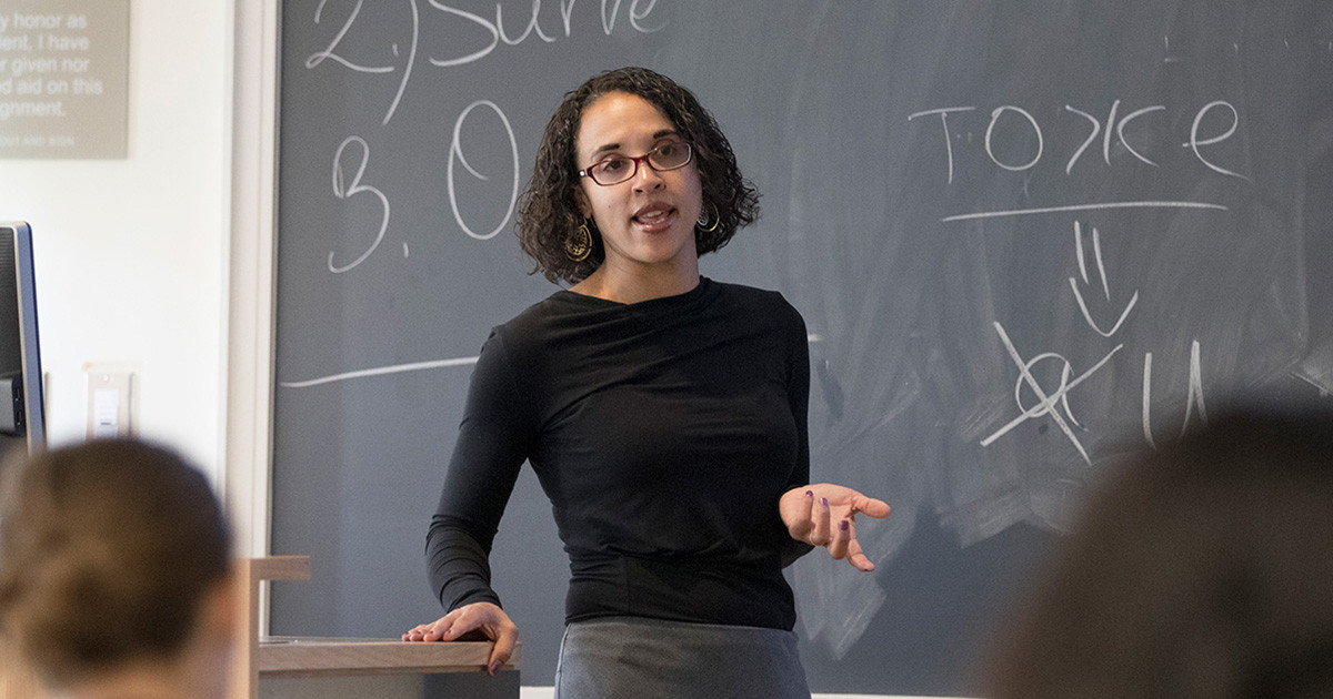 Female professor smiling and pointing to a student in the classroom