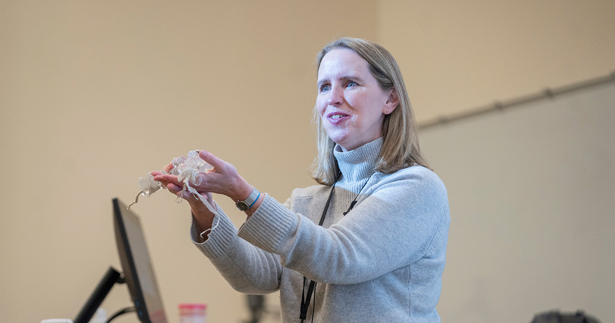 Young professor standing with arms outstretched while holding medical supplies in hands.