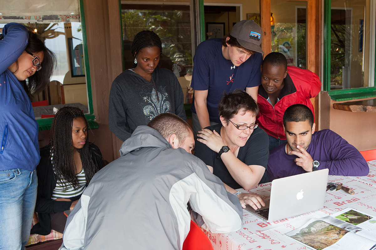 Female professor looking at a laptop while surrounded by students and community members.
